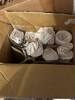 Top view of cardboard box containing multiple clear glass wine glasses, some wrapped in paper for protection.