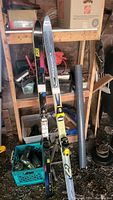 Two sets of skis including one pair of Elan Spitfire and one pair of Rossignol skis positioned against shelving with tools in the background, showing overall condition and bindings attached.