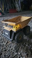 Front-side view of the antique toy dump truck showing the yellow cab, front grille, and dumping bed with large tires.