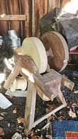 Side view of large antique grinding stone wheel showing wooden frame, stone wheel, and adjacent wooden piece.