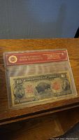 Front view of novelty $10 gold banknote sealed in original plastic packaging with certificate of authenticity.