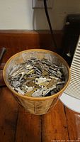 Photo showing the wicker bin filled with a large number of assorted metal keys of various types and sizes from a top view.