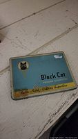 Closed view of the Black Cat Virginia Cigarettes tin on a wooden surface showing the front lid design.