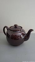 Front side view of large brown glazed ceramic Brown Betty teapot on neutral background.