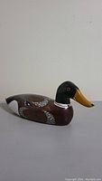 Side view of one wooden decoy duck showing detailed painting and carving with yellow bill, dark green head, and brown body with feather patterns.