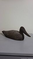 Side view of carved wooden duck decoy showing shape and wear