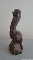 Side view of the hand carved wooden pelican statue showing the full body and base with bark.
