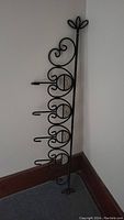Full view of black metal hanger rack standing upright by the wall, showing five hooks and decorative scrollwork.