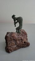 Metal figurine shaped like an abstract animal standing on a rough volcanic rock.