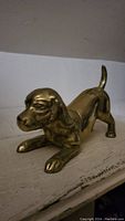 Front side view of the vintage brass dog figurine depicting the detailed head and front paws bent on surface