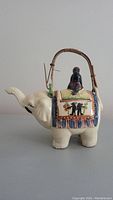 Side view of vintage elephant ceramic teapot showing handle, spout, and rider figurine on top