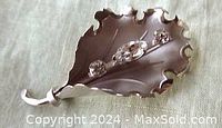 Front view of the leaf-shaped sterling silver brooch showing three clear rhinestones prong set on the curved surface with scalloped edges.