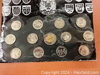 Photo of 14 Canadian commemorative coins in a black folder with provincial shields and the Canadian coat of arms at top.