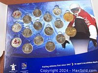 Photo of 17 commemorative coins mounted in a presentation folder depicting various Winter Olympic sports and an athlete dressed in red on a blue background