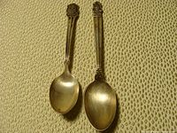 Two sterling silver spoons placed side by side showing front profile on textured beige fabric.