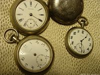 Four pocket watches laid out showing dials and cases