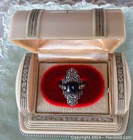 Art Deco single ring showcased in a decorative vintage-style ring box with a cream-colored exterior and red velvet interior.