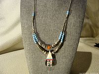 Full view of the necklace displayed on a gray stand, showing double strands of turquoise and silver beads with the teardrop pendant.