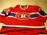Full view of the front of the red Montreal Canadiens hockey jersey with blue and white stripes and central team logo.