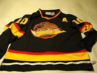 Full front view of black Vancouver Canucks jersey with Pavel Bure #10, with measuring tape across the bottom hem showing width