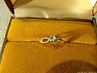 Ring in open presentation box from top angle showing aqua-colored stone and infinity loop band design