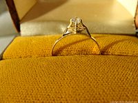 Close-up of 9K gold ring with clear stone set in six prongs on yellow fabric inside box.