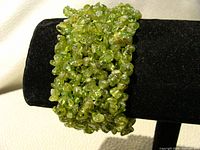 Close-up view of the peridot chip bead stretch bangle on a black stand showing the detail and texture of the beads.