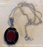 Front view of the oval sterling silver pendant with inlaid black stone and flat red carnelian stone center on the chain.