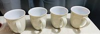 Four cream-colored Denby coffee mugs lined up next to each other, showing front and handles.