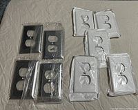 Photo showing assorted black and white new dual outlet receptacle covers in original packaging.