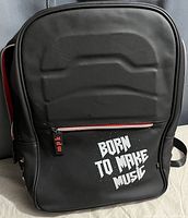 Front view of black knapsack with padded top and 'Born to Make Music' text on zipper pocket.