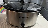 Side view of the Bravetti slow cooker showing stainless steel and black accents, control knob, and glass lid.