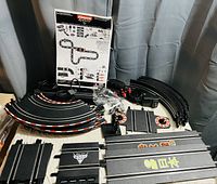 Multiple Carrera GO!! slot car track pieces arranged on a surface including curved, straight track sections, controllers, power cable, and instruction sheet.