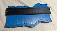 Top-down photo of the duplicator measuring tool showing the black base with ruler markings and blue adjustable pins.