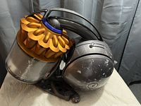 Dyson vacuum cleaner body showing gold cyclone dustbin with black and gray canister base, visible scratches and wear.