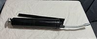 Photo showing black lever-style grease gun lying on a white surface, highlighting metal lever and bent nozzle.