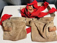 View of the entire tool pouch with multiple pockets and attached red suspenders on a white surface.