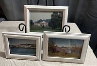 Three white-framed prints arranged on a stand, showing different scenic images as described.