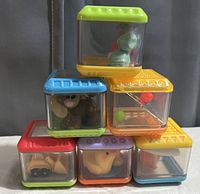 Photo of six Fisher-Price Peekaboo sensory stacking blocks showing colorful lids and small animal or object figures enclosed in transparent cubes.