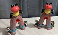 Pair of vintage tin ladybug wind-up toys, each with red body, striped legs in blue and orange/red, yellow collar, black antennae and small silver bells attached to legs