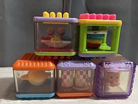 Six colorful Fisher-Price Peekaboo sensory stacking blocks shown in two rows with various interactive and sensory features inside transparent sides.