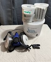 SAS respirator mask with cartridges and three white containers labeled Ark Composites epoxy resin and hardener, partially full.