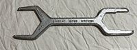One photo showing a silver metal spud wrench with two different sized open-end wrench heads and a tapered spike on one end.