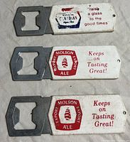 Three vintage Molson Canadian and Export Ale metal bottle openers laid out flat