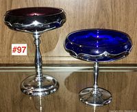 Two Mid-Century Modern pedestal tazzas by Farber Bros. shown side by side on shelf, one amethyst and one cobalt blue glass bowl with silver pedestal bases.