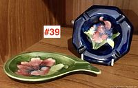 Green leaf-shaped ashtray and blue octagonal ashtray displayed together on wood surface