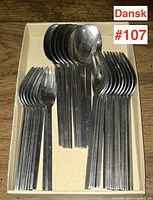 Top down photo showing multiple stainless steel forks and spoons arranged neatly in a box labeled 'Dansk #107'.