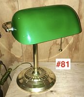 Front and side view of brass banker’s lamp with green glass shade on wooden surface.