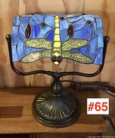Frontal view of the desk lamp's leaded glass shade showing a dragonfly design in colors blue, yellow, red and black.