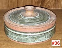 Closed view of the circular lidded ceramic box showing greenish glaze and natural clay rim and lid knob.